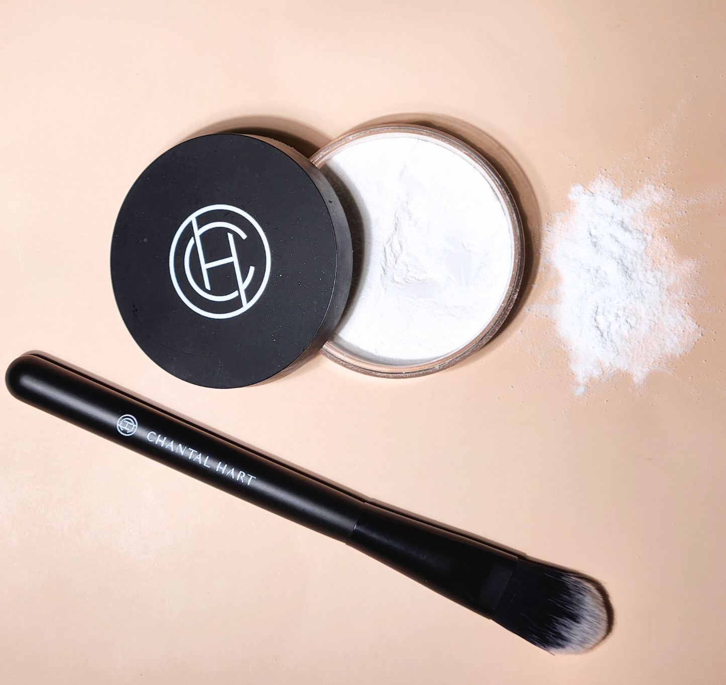 A jar of loose powder with its lid off, alongside a black makeup brush, displayed on a beige background.