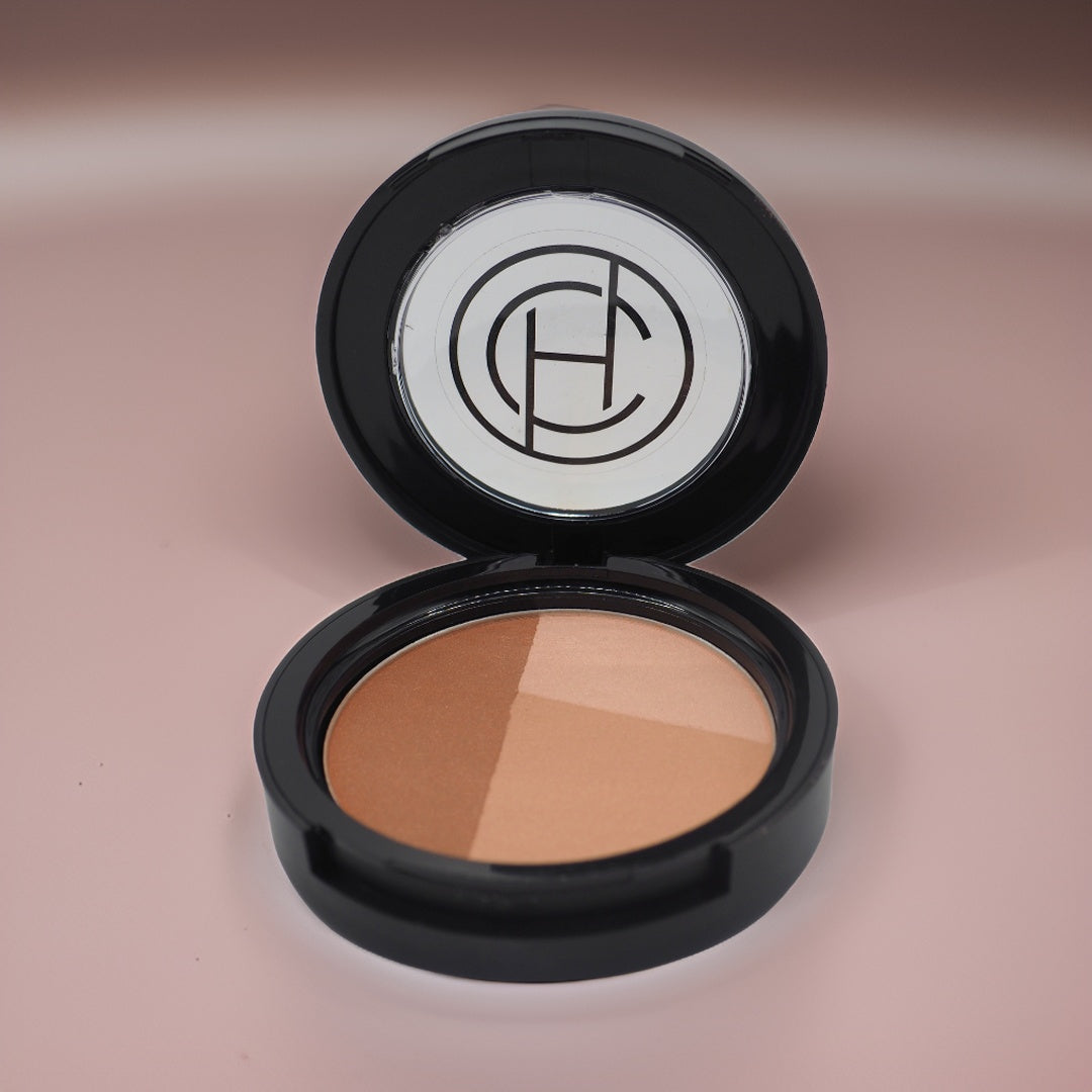 A compact pan with three shades of tri-colored bronzer, with a mirror in the center of the compact showing the Chantal Hart brand logo.