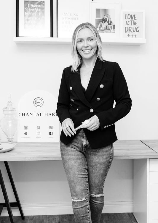 Chantal Hart in a black blazer and jeans standing in an office setting with framed pictures on the wall.