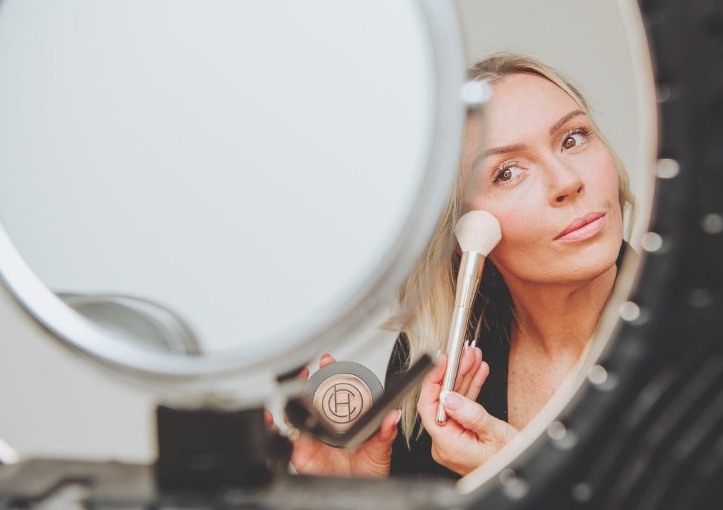 Chantal Hart applying makeup in front of a mirror, with a focus on the reflection of the face in the mirror.